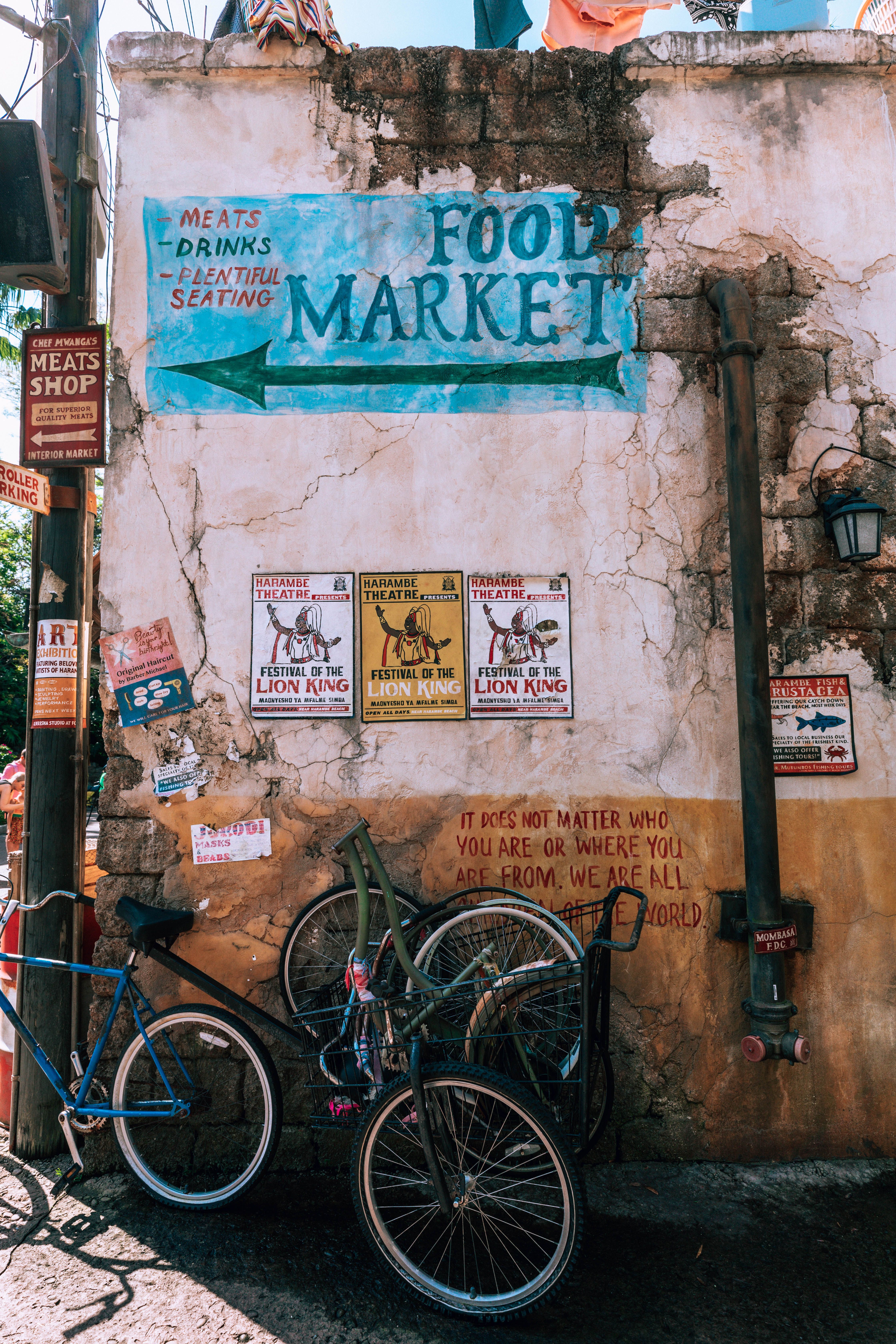A painted wall in Tulum town: a food market sign with a hand-painted arrow, three Festival of the Lion King posters, and graffiti reading \u2018It does not matter who you are or where you are from. We are all citizens of the world.\u2019