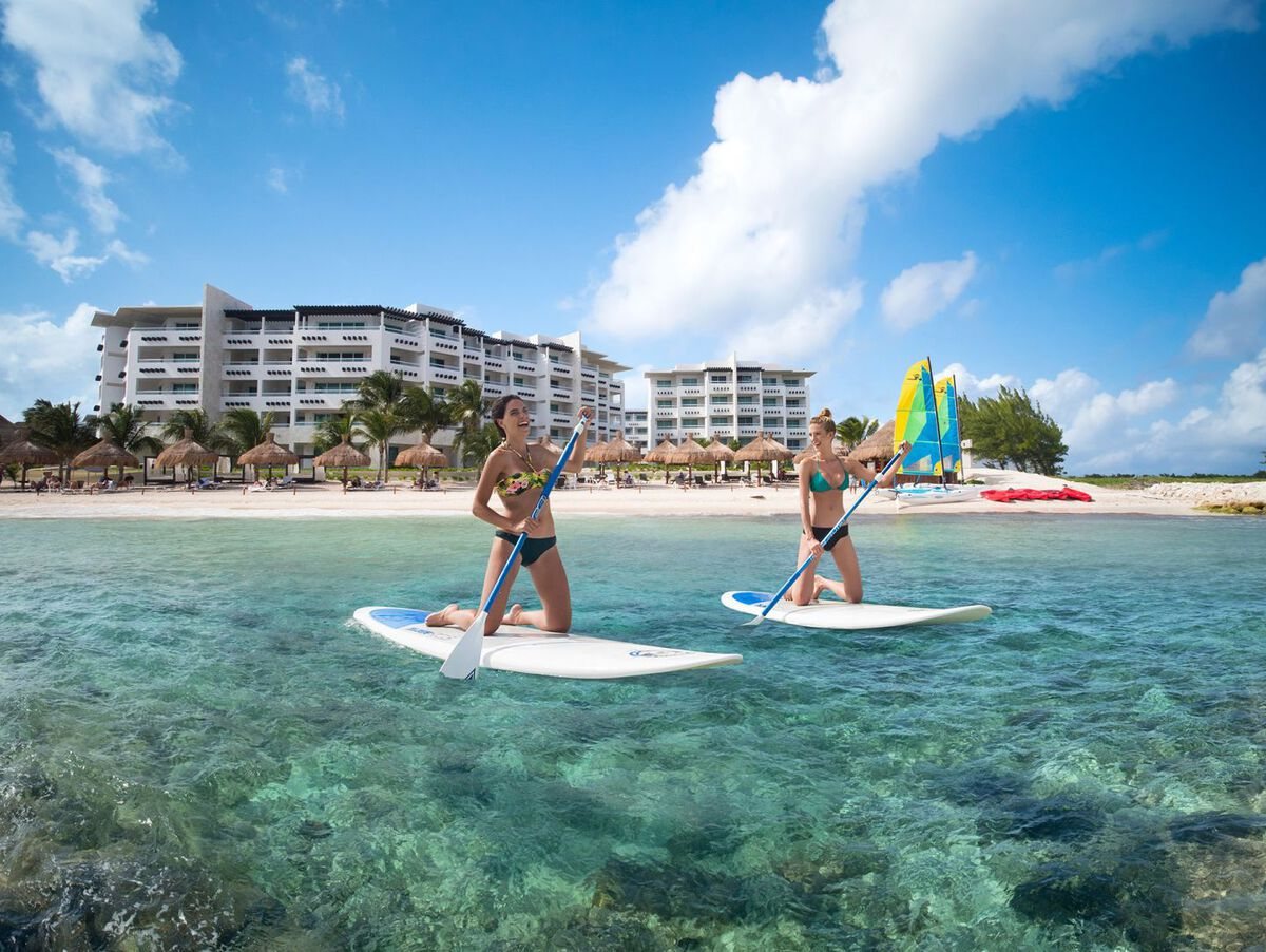 Two people paddleboarding in clear turquoise water in front of Ventus at Marina El Cid